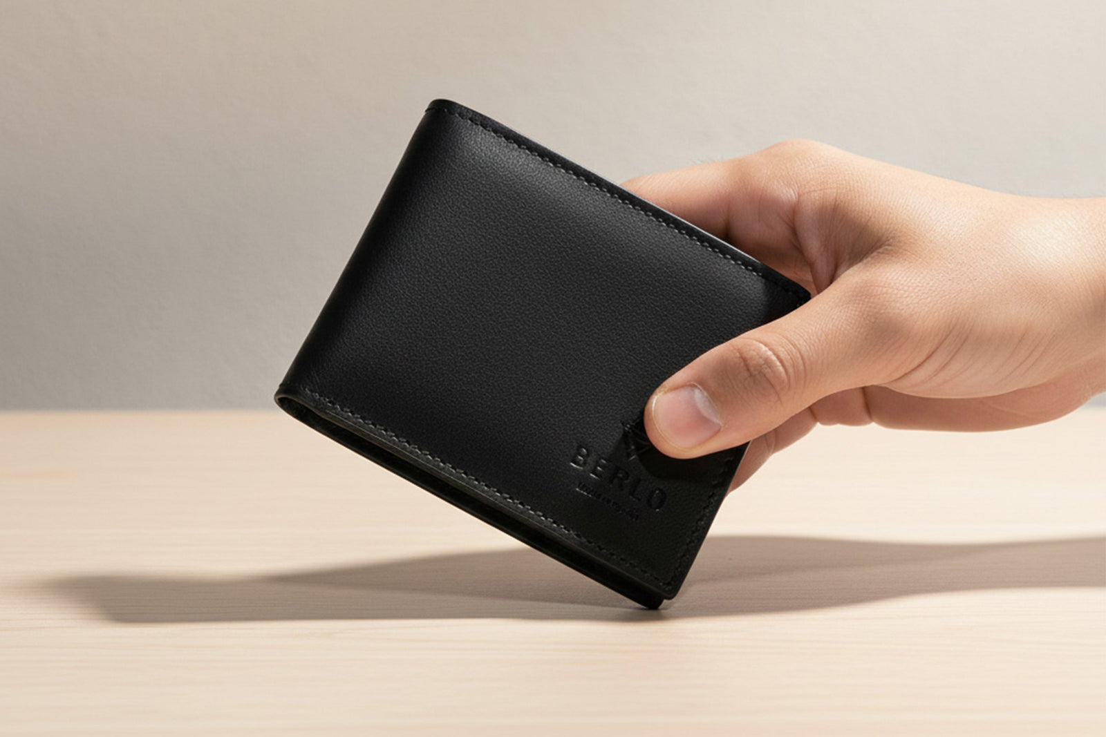 A sharp, high-contrast shot of a Berlo wallet held in a hand. The lighting highlights the matte texture and the precision of the hand-painted edges. Minimalist background.
